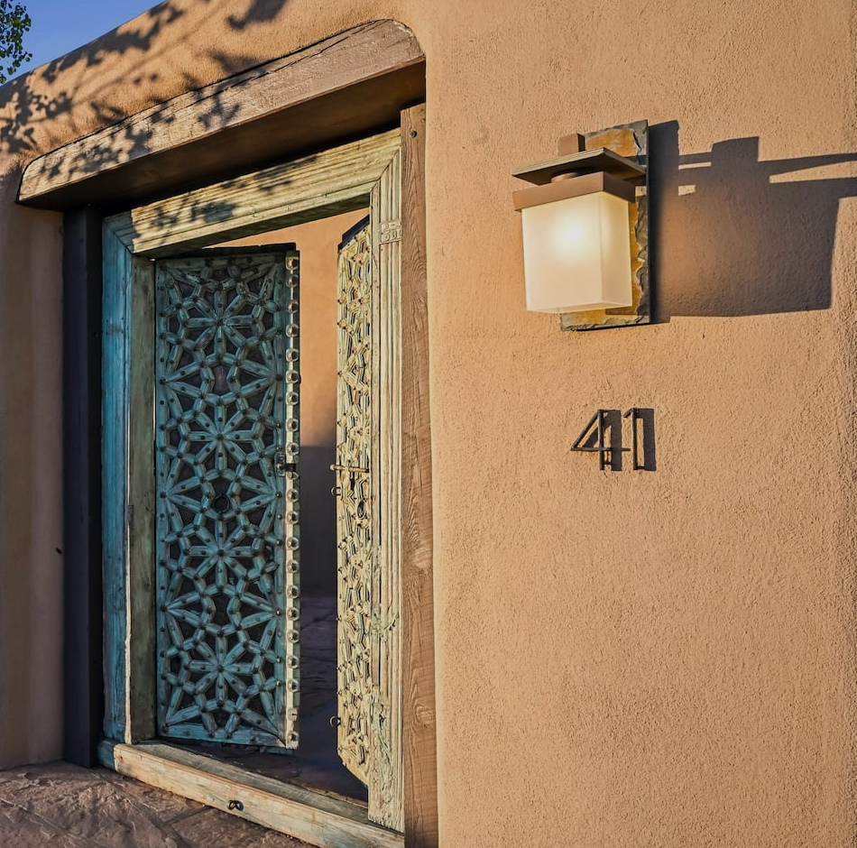 Carved verdigris gates opening into Casa Verdigris, framed by warm adobe and a glowing lantern